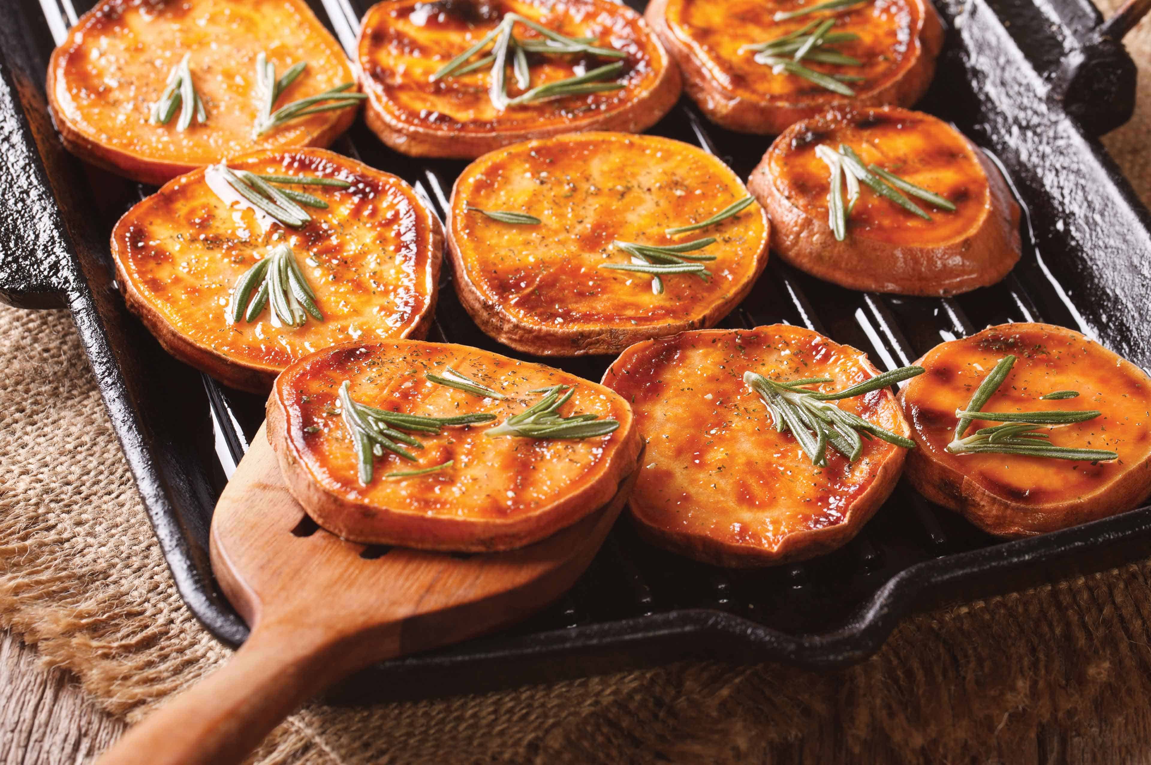 Grilled sweet potato slices with rosemary on a skillet.