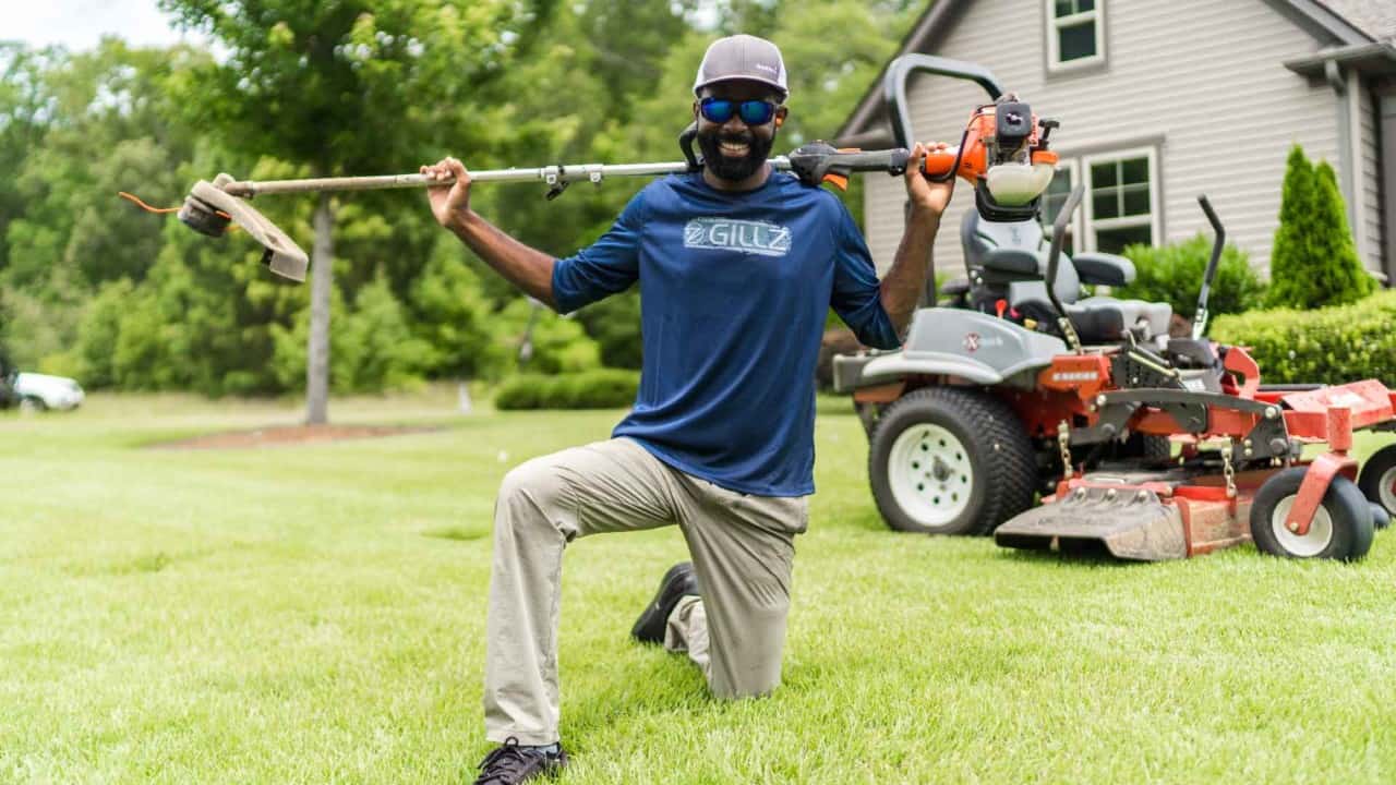 Brian Latimer holding lawn tools with Exmark mower behind him