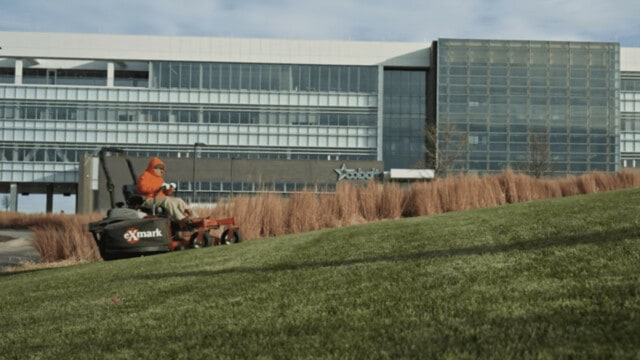 Man on Exmark mower mowing up a hill in front of a corporate building