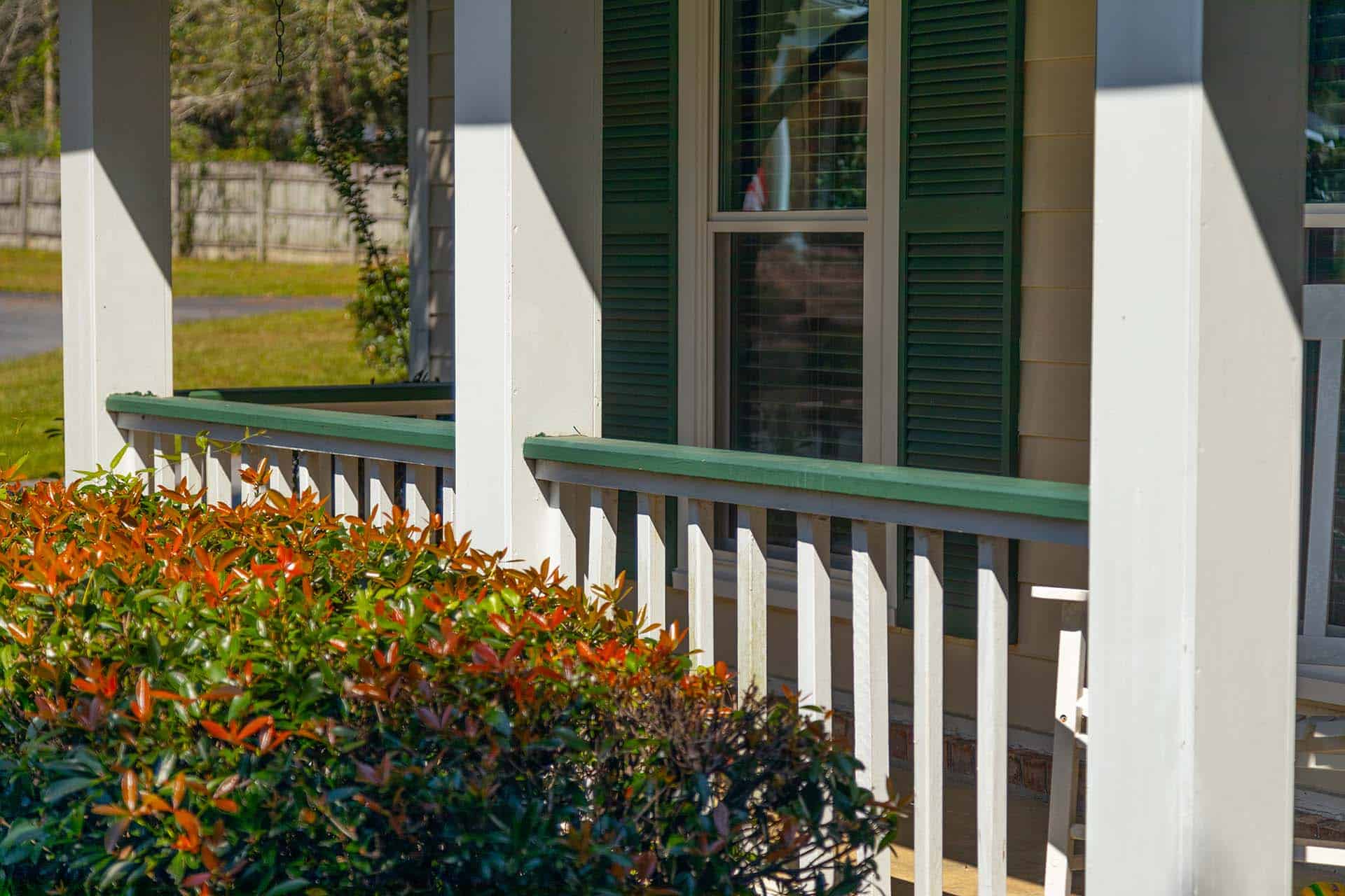 A painted front porch railing with bushes in front
