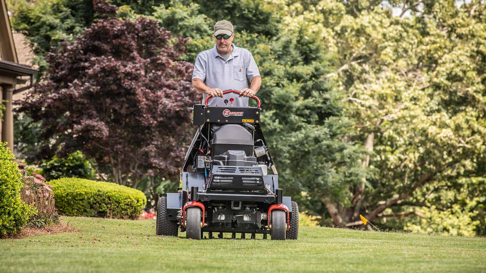 Man standing on aerator using it in yard